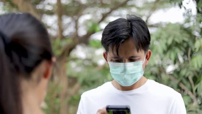 年轻的亚洲男子使用智能手机和佩戴防护面具，以防止细菌和空气污染，保健概念