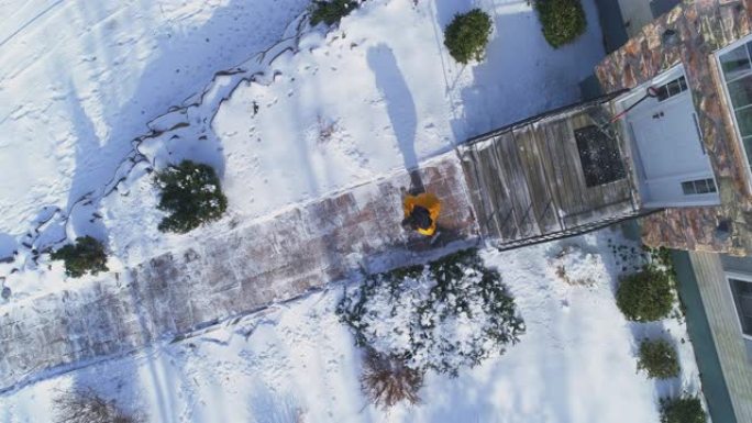 一名身穿黄色夹克的50岁成年长发男子扫过小路，在一场冬季降雪后，将乡间别墅前院的积雪从积雪中扫走。