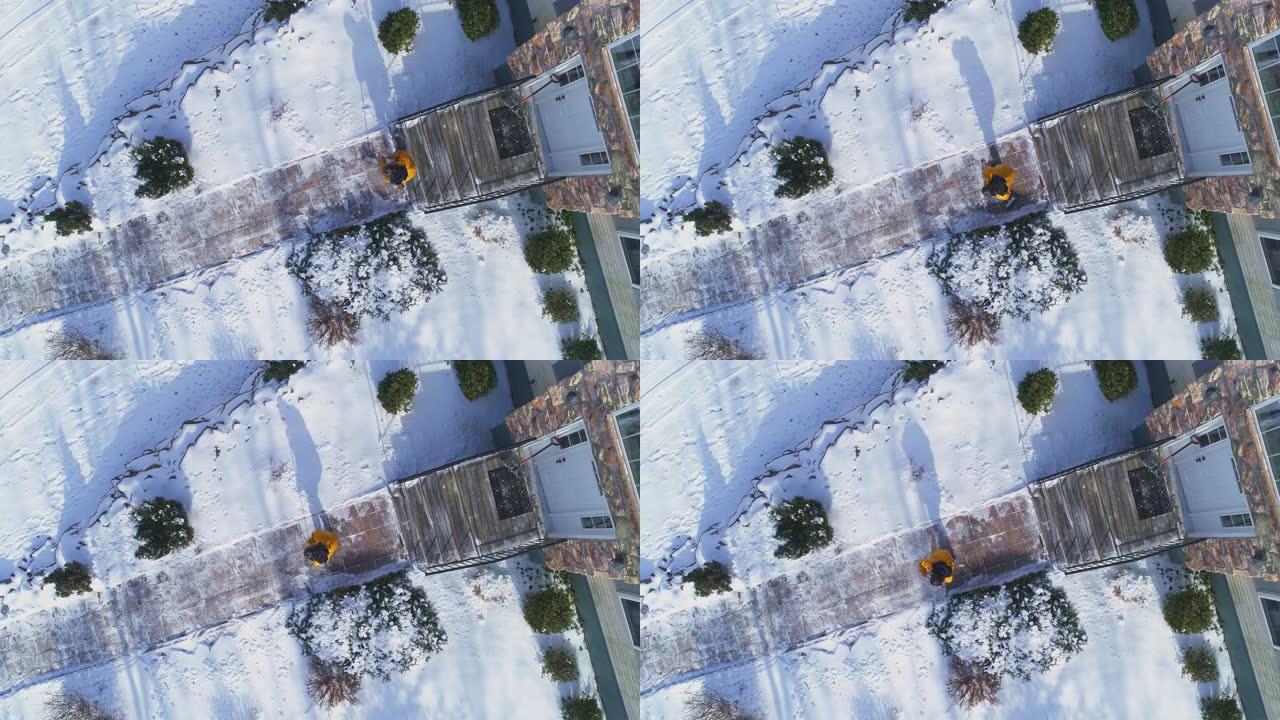 一名身穿黄色夹克的50岁成年长发男子扫过小路，在一场冬季降雪后，将乡间别墅前院的积雪从积雪中扫走。