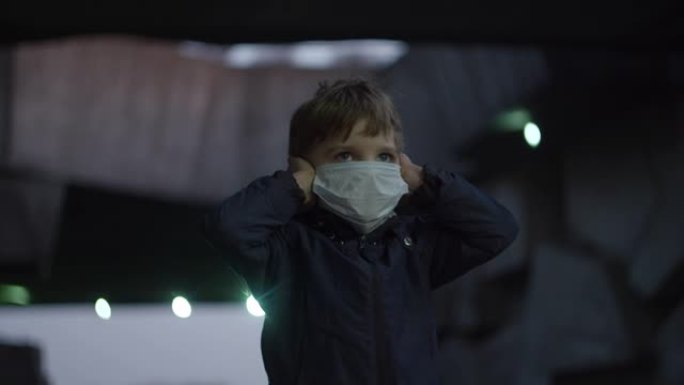 戴着医用防护面具的男孩在冠状病毒新型冠状病毒肺炎大流行期间站在避难所里，周围有害怕的手表。由于室外红