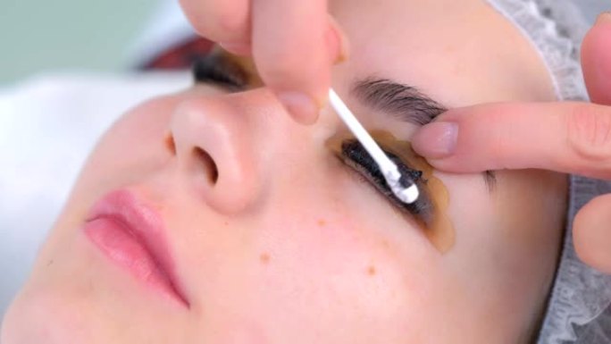美容师在绘画过程中从女孩的睫毛中擦拭溶液。