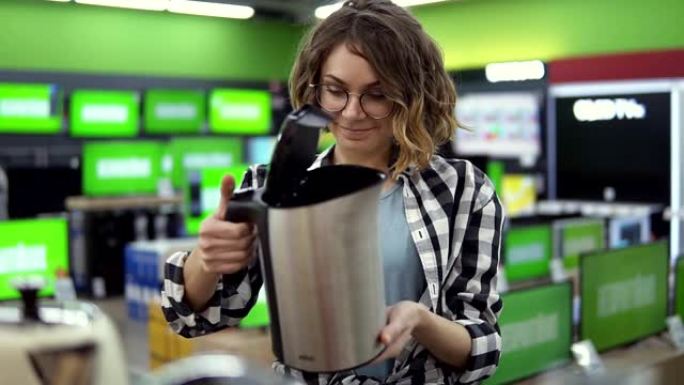 一位穿着格子衬衫、戴着眼镜、乐观开朗的年轻女士在家用电器商店里挑选一个电子水壶，从货架上拿了一个，并