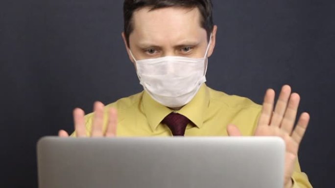 一名戴着医用口罩的男子打开一台笔记本电脑，并通过互联网参与交流。手势广泛，向对话者展示喉咙喷雾。冠状