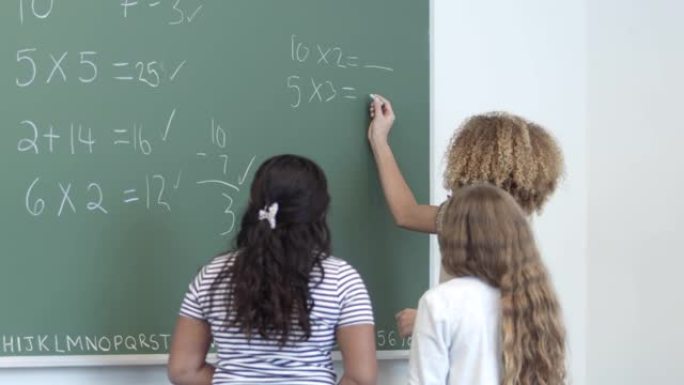 一群小学年龄的女孩一起在黑板上写下数学问题的答案