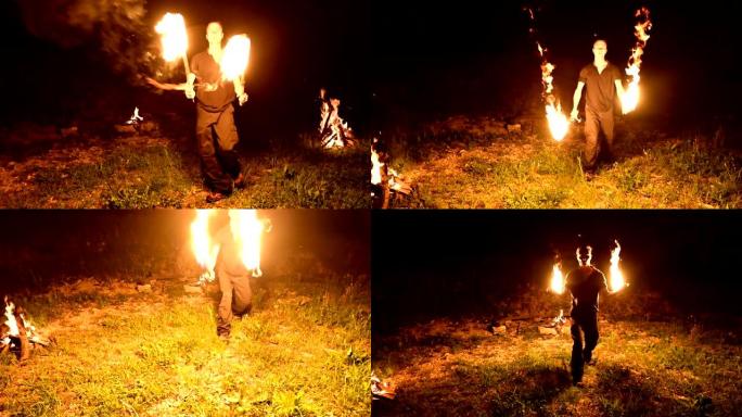 低调。长发的年轻男性在黑色夜晚视频慢动作中旋转燃烧的火炬。现代法克尔 (fakir) 用燃烧的员工做