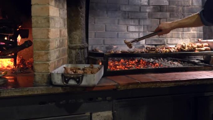 古老的意大利传统技术，在砖炉的烧烤架上烤切成薄片的肉，男厨师使用食物钳，并将美味的肉排放在金属炉排上