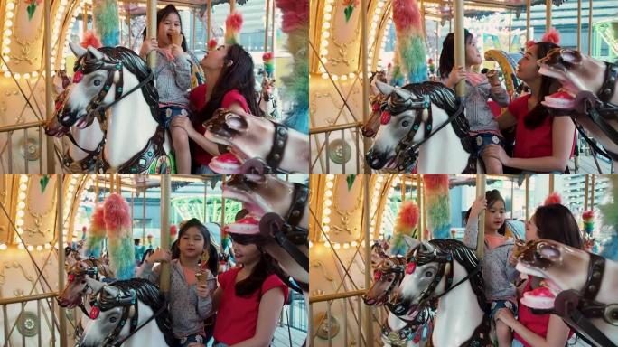 享受游乐园的概念。亚洲其他人和她的女儿一起骑着旋转木马，微笑着在集市或游乐园里玩得开心。