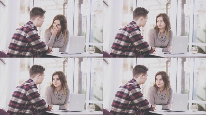 可爱的女孩坐在咖啡馆的桌子旁。她正在与男友交流，男友正在笔记本电脑上给她看东西。集中情侣。特写。复制