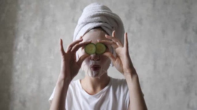 一个戴着口罩的女人正在玩圆形黄瓜，看着相机，鬼混。自然再生护肤