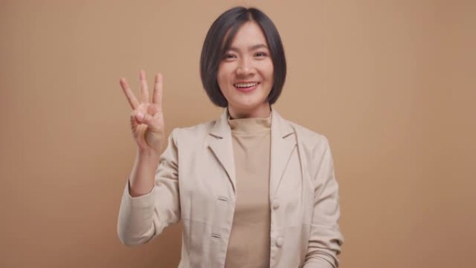 亚洲女商人显示用手指计数数字，微笑孤立在米色背景。4k视频