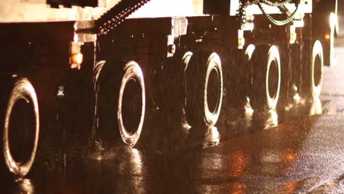 晚上在雨中运送大件货物的卡车。道路上轮胎的特写