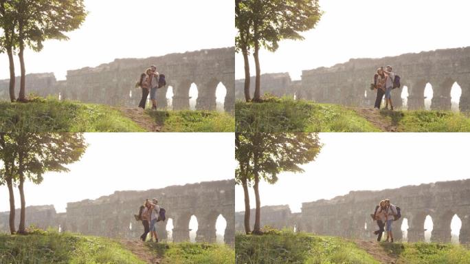年轻可爱的夫妇背包客游客在罗马水道拱门前的山上自拍照片，罗马公园废墟上浪漫的迷雾日出慢动作