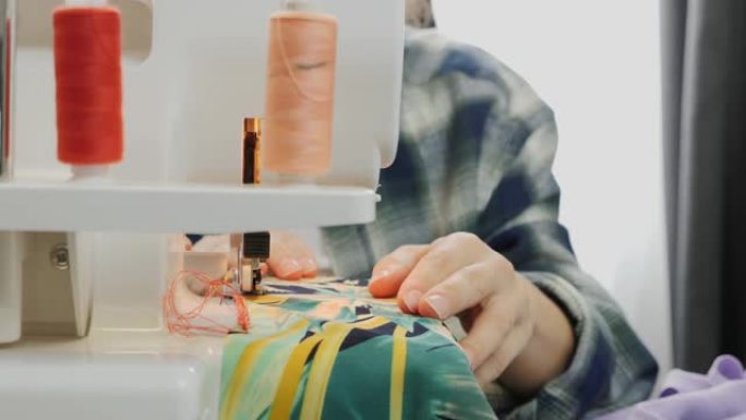 女人的手的特写工作在缝制织物的包锁上。缝纫机的特写。包锁机的细节。女性正在缝制衣服。创造和剪裁服装概