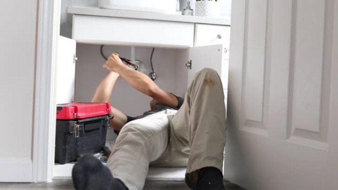 从门口看到，年轻的男性水管工坐在地板上，并更换了浴室水槽下的陷阱管