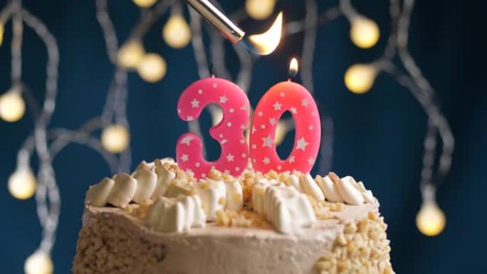 蓝色背景上有30号粉色蜡烛的生日蛋糕。蜡烛着火了。慢动作和特写视图