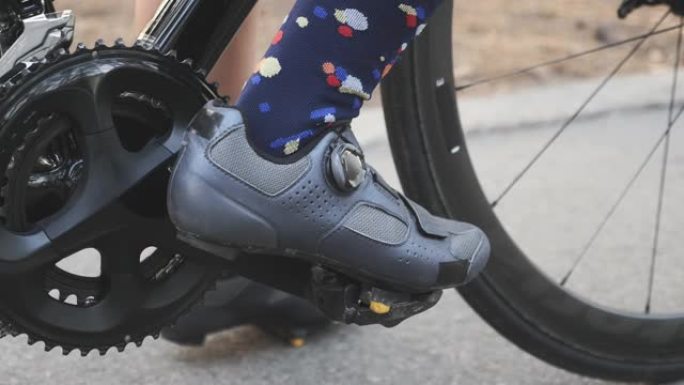 骑自行车的女孩在比赛训练前将脚踏板上的公路鞋夹在脚踏板上。链环和自行车特写。慢动作