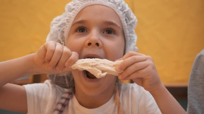 戴着一次性帽子的小女孩在厨房玩生面团。快乐的女孩手握面团在烹饪学校的烹饪大师课上。
