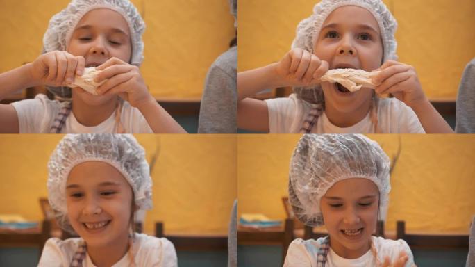 戴着一次性帽子的小女孩在厨房玩生面团。快乐的女孩手握面团在烹饪学校的烹饪大师课上。