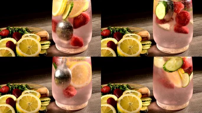 玻璃水瓶中的特写镜头是柠檬片和黄瓜，薄荷和冷冻草莓在苏打水中搅拌。在柠檬水玻璃器皿中旋转水果