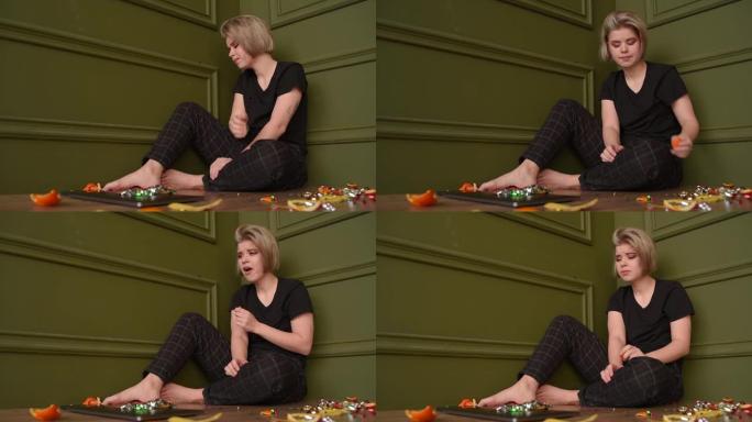 一个不快乐的女孩坐在地板上痛苦地吃着五彩纸屑和橘皮。拍摄剪辑。