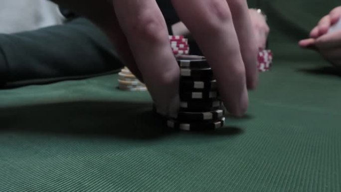 在绿布背景下的扑克牌桌上使用扑克筹码的男性手的特写镜头。休闲的概念
