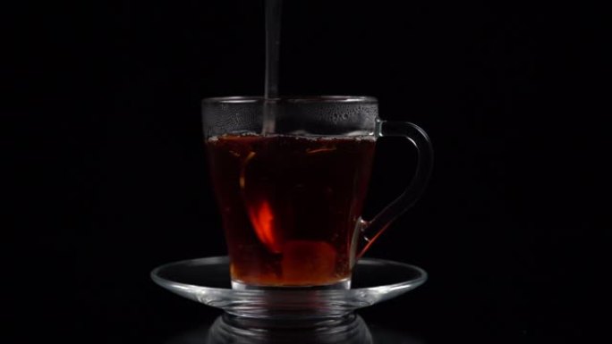 一块蔗糖放入热茶中，并用茶匙在黑色背景上的茶杯和茶碟中搅拌，慢动作