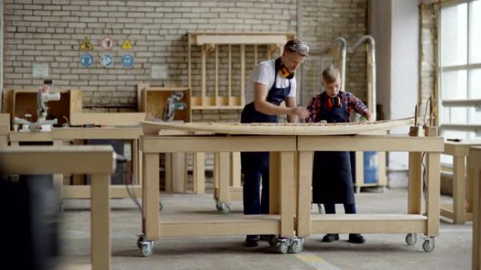 中年木匠教儿子如何在木工车间的工作台上制作木船