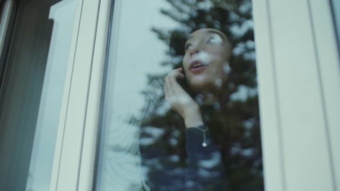 年轻女子在窗户附近的电话上讲话