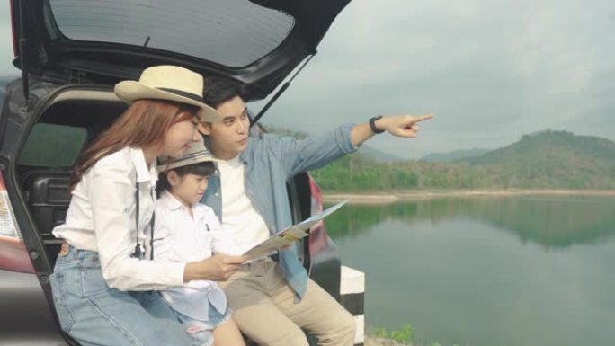 亚洲家庭的肖像坐在车里，父亲指着风景，母亲带着女儿在度假时一起看着美丽的风景，拿着地图。幸福的家庭时