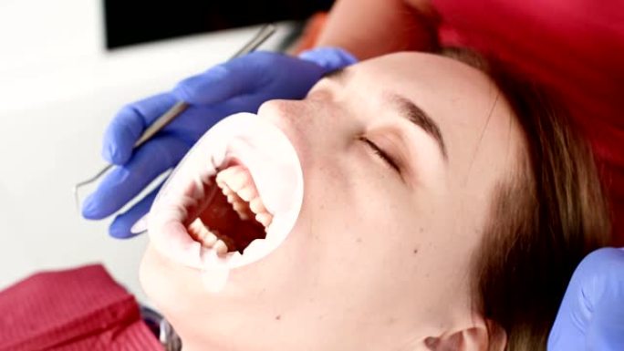 牙科检查员张开嘴，用餐巾纸和闭着眼睛检查女孩的脸部特写。带有检查工具的牙医手