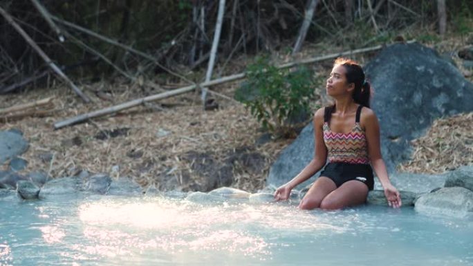 无忧无虑的年轻女子坐在温泉中的岩石上。