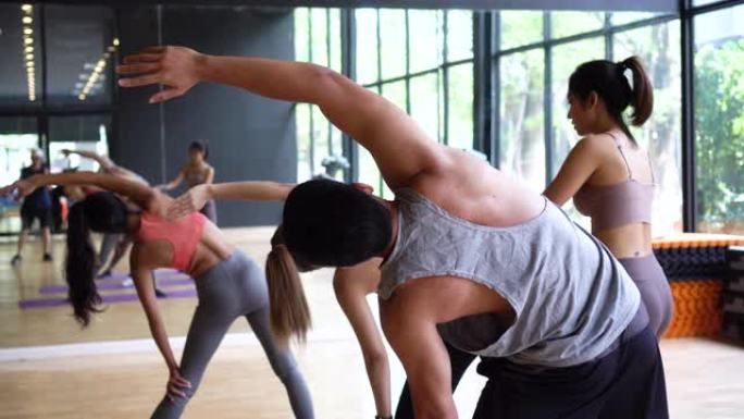 亚洲年轻瑜伽女教练协助男性初学者平衡灵活性在健身房的课堂上摆姿势
