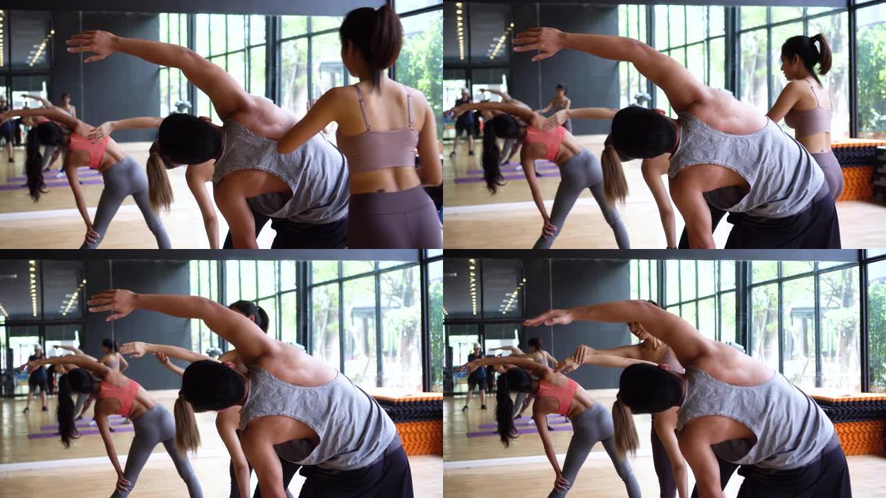 亚洲年轻瑜伽女教练协助男性初学者平衡灵活性在健身房的课堂上摆姿势