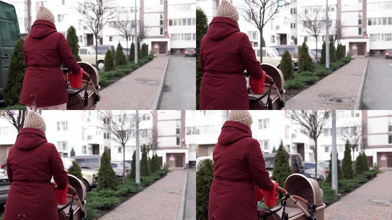 一位年轻的母亲带着婴儿车走在街上。母性的概念。