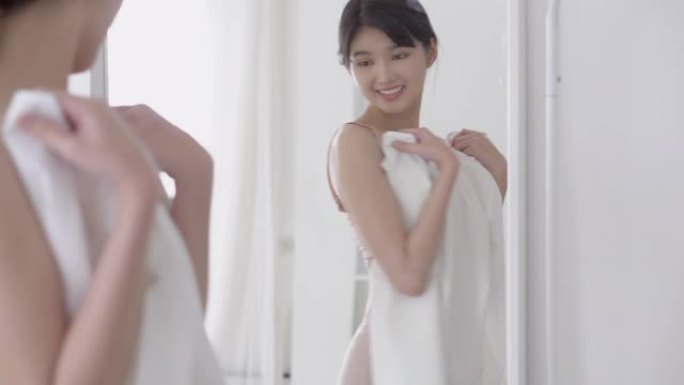 美丽的年轻亚洲女人穿着内衣快乐拿着连衣裙照镜子在家休息，穿着内衣的美女亚洲女孩性感身材合身，在房间里