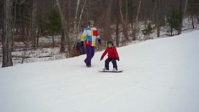 年轻人滑雪板教练tiches小男孩如何骑滑雪板。冬季活动概念。慢动作镜头