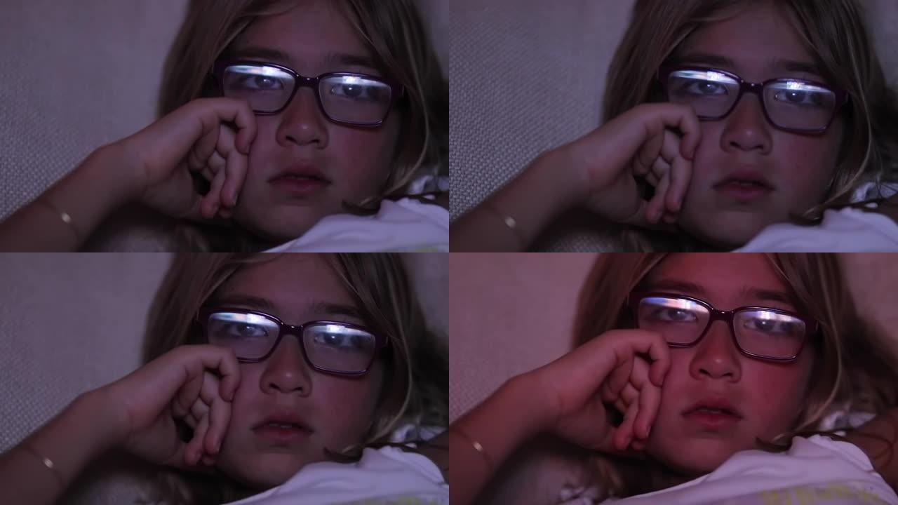 儿童晚上看电视屏幕的特写戴眼镜的小女孩