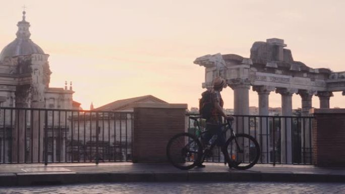 年轻人游客背着背包和自行车在日出时在罗马广场散步。从全景的角度来看，意大利罗马的历史帝国罗马罗马。