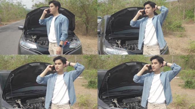 亚洲年轻的不快乐男子在乡村公路上开着的引擎盖抛锚的汽车前用手机打电话寻求帮助。旅途中的破车在路上。
