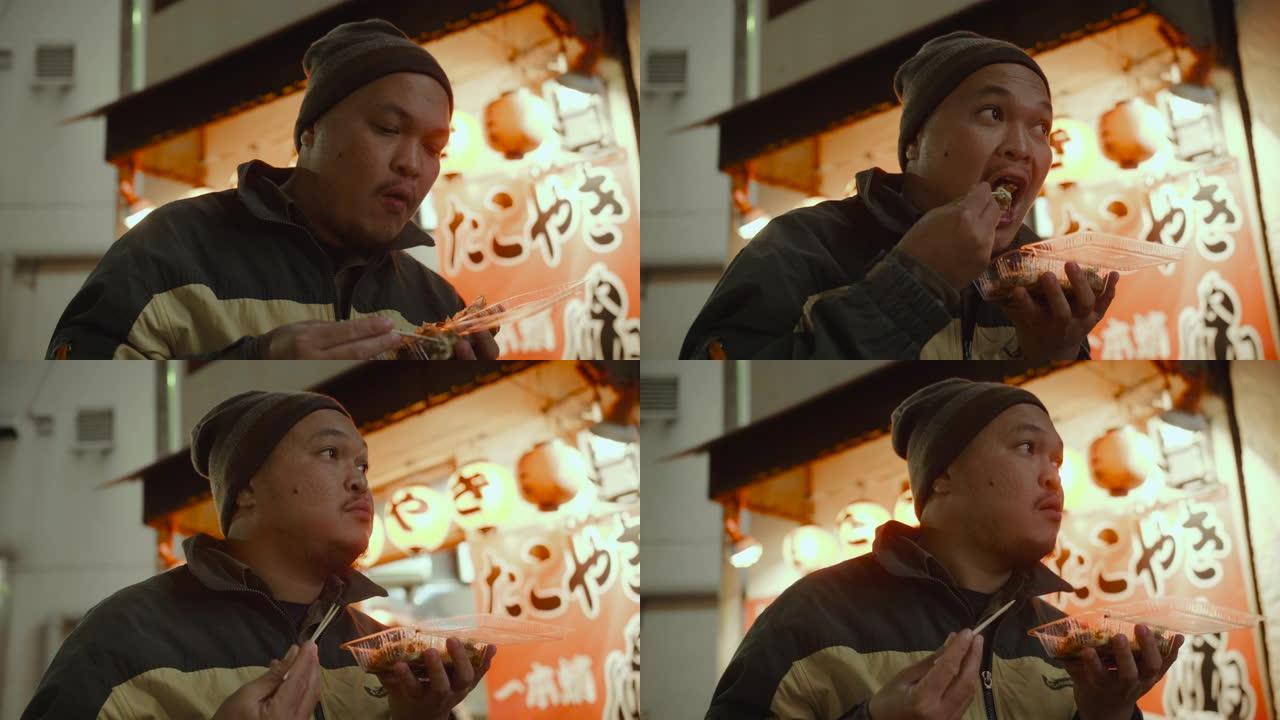 亚洲旅游男子晚上在城市街道吃日本食物章鱼烧。