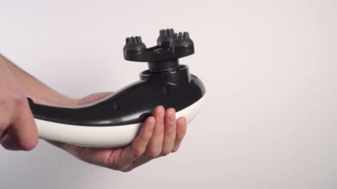 一个年轻人用带有凸起喷嘴的黑色白色电动振动按摩器敲他的手