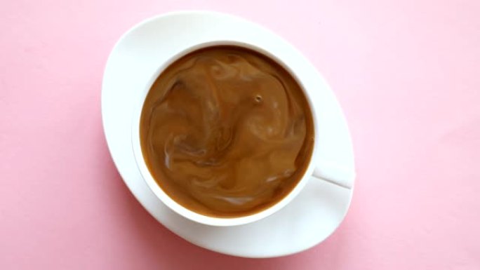 用手将牛奶倒入咖啡中，在粉红色背景的杯子中混合咖啡和牛奶