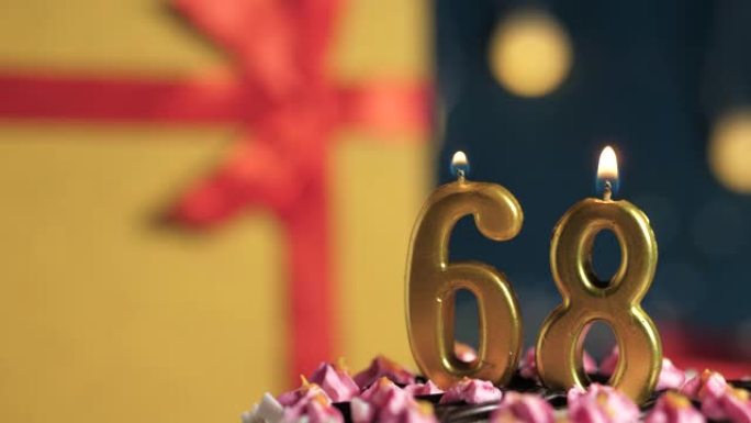 生日蛋糕68号点火器燃烧的金色蜡烛，蓝色背景礼物黄色盒子用红丝带绑起来。特写和慢动作
