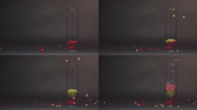 蓝色糖果落在玻璃花瓶中的粉色、红色和绿色糖果上慢动作，黑色黑板纹理背景上的复制空间