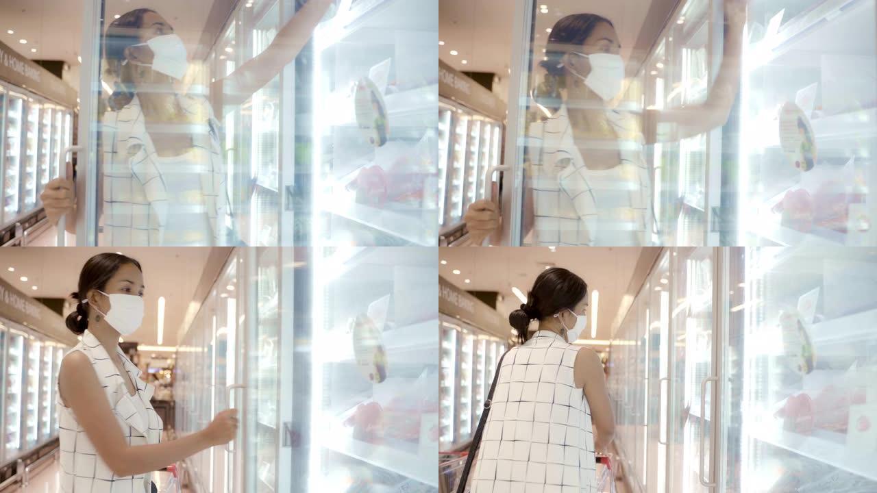 年轻的亚洲女性从超市商店的深冰柜中挑选产品，面罩保护灰尘和病毒健康。