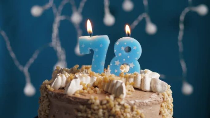 蓝色背景上有78号蜡烛的生日蛋糕。蜡烛吹灭了。慢动作和特写视图