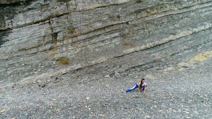 女人在岩石背景上进行呼吸练习时深蹲和伸展身体弯曲。空中美丽的镜头视图。
