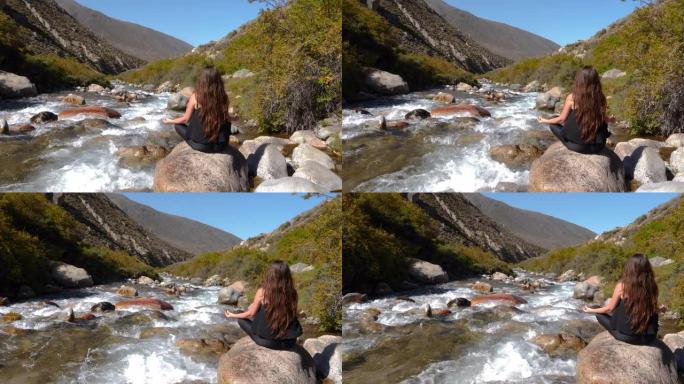 妇女练习冥想做瑜伽在急流河和山脉的后视图。