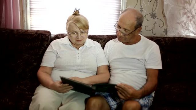 成年夫妇坐在沙发上看着他们的照片。夫妻戴着眼镜看他的专辑。