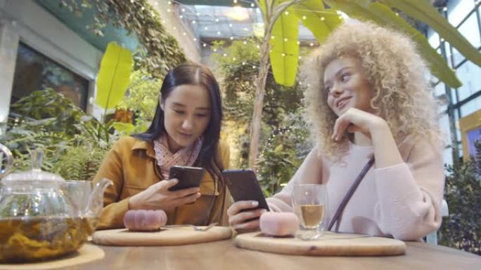 两名使用智能手机并在咖啡馆讲话的年轻女性